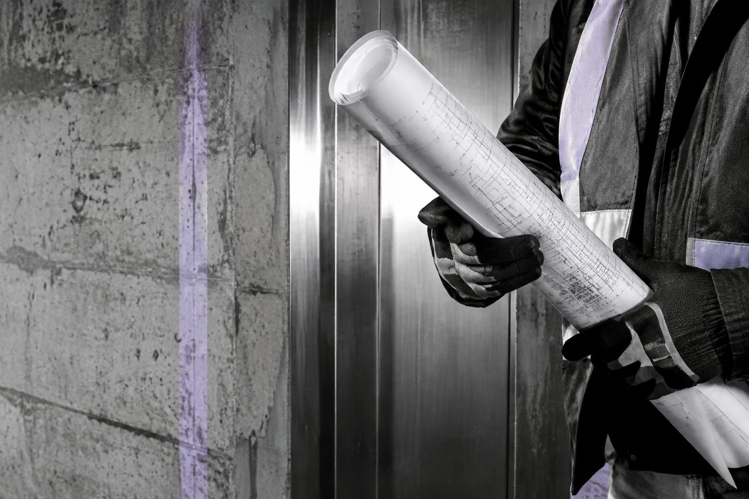 Construction professional holding plans beside raw concrete and steel